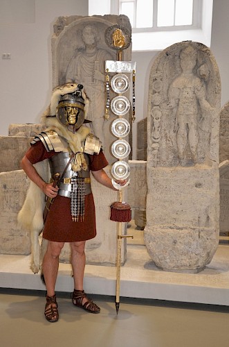 Der schlechte Erhaltungszustand des Steins und der unproportionierte Körper mit stark abgewinkelten Armen und großem Kopf machen es schwierig, sich ein richtiges Bild von Caius Valerius Secundus zu machen. Eine Vorstellung von seinem Aussehen gibt ein Mitglied der 1. Römercohorte Opladen.